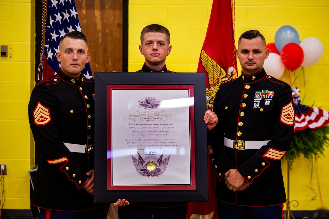 Pfc. Gavin G. Northcutt, holds the Honorary Marine award (posthumously) for his cousin Hunter A. Northcutt next to Staff Sgt. James B. Benham (left) and Gunnery Sgt. Nathan D. Mitchaner (right), the local Marine Corps recruiters, at Pelham Elementary School, Pelham, Tennessee, June 13, 2018. Hunter was in line to carry on the family tradition of being a United States Marine, unfortunately, his terminal leukemia ended his life before he could stand on the yellow footprints. (U.S. Marine Corps photo by Sgt. Mandaline Castillo)