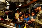 Machinery Repairman 3rd Class Samuel Lopezclemente gives the Mayor of Piti, Jesse Alig, and students from various schools participating in the Piti Summer Program a tour of the machine shop during a ship tour aboard the submarine tender USS Frank Cable (AS 40), June 18. Frank Cable, forward-deployed to the island of Guam, repairs, rearms and reprovisions submarines and surface vessels in the Indo-Pacific region.