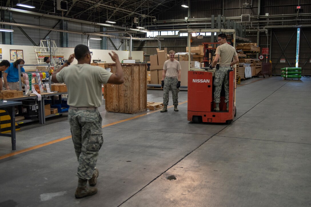Tech. Sgt. Edwin Jacobo, 374th Logistics Readiness Squadron NCO in charge of outbound cargo, directs Airman 1st Class Boaz Rogel, 374th Security Forces Squadron patrolman, as he maneuvers a package with a forklift during a Wing Immersion program at Yokota Air Base, Japan, June 20, 2018.