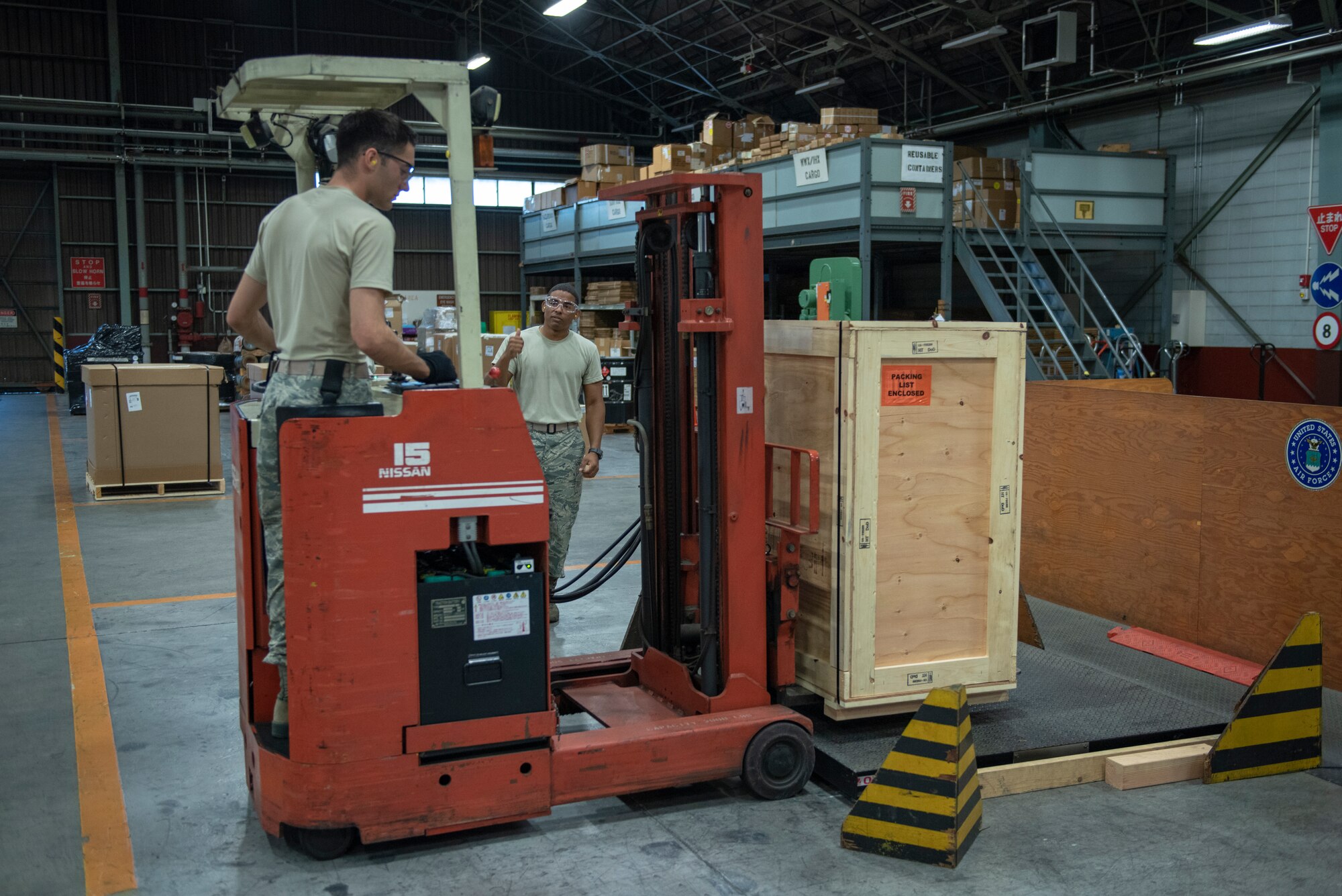 Tech. Sgt. Edwin Jacobo, 374th Logistics Readiness Squadron NCO in charge of outbound cargo, directs Airman 1st Class Boaz Rogel, 374th Security Forces Squadron patrolman, as he maneuvers a package onto a scale to be weighed before shipment during the Wing Immersion program at Yokota Air Base, Japan, June 20, 2018.