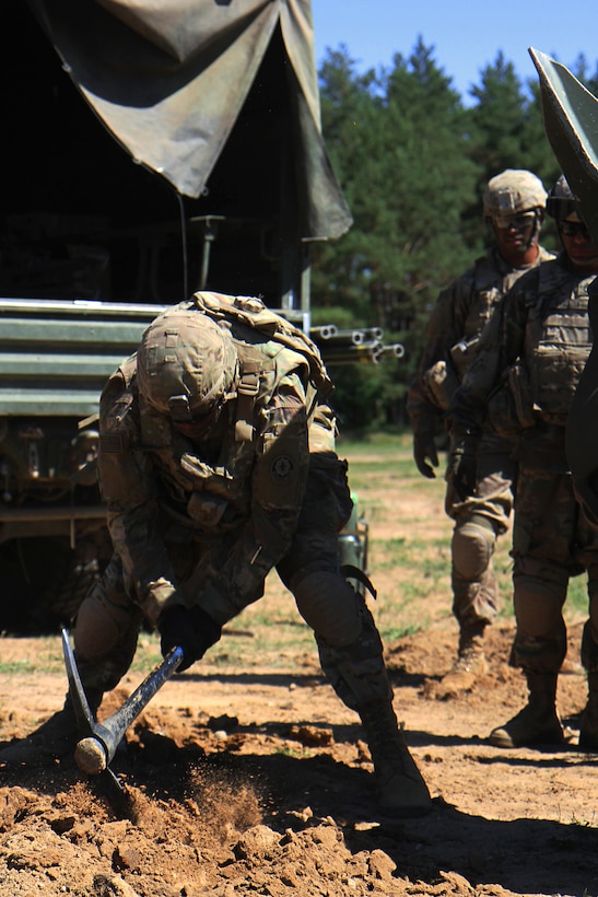 A soldier uses a pickax to prepare a site for a howitzer.