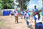 Volunteers, students, and U.S. service members clean up trash.