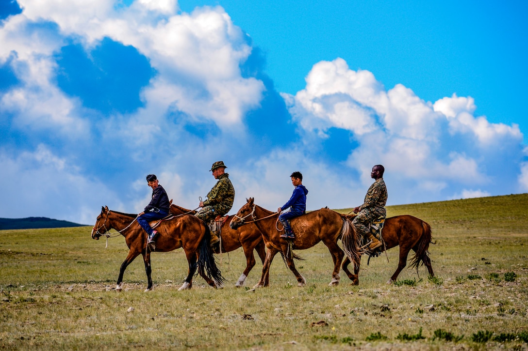 Two Marines and two youths ride horses in a line.