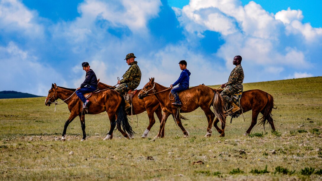 Two Marines and two youths ride horses in a line.