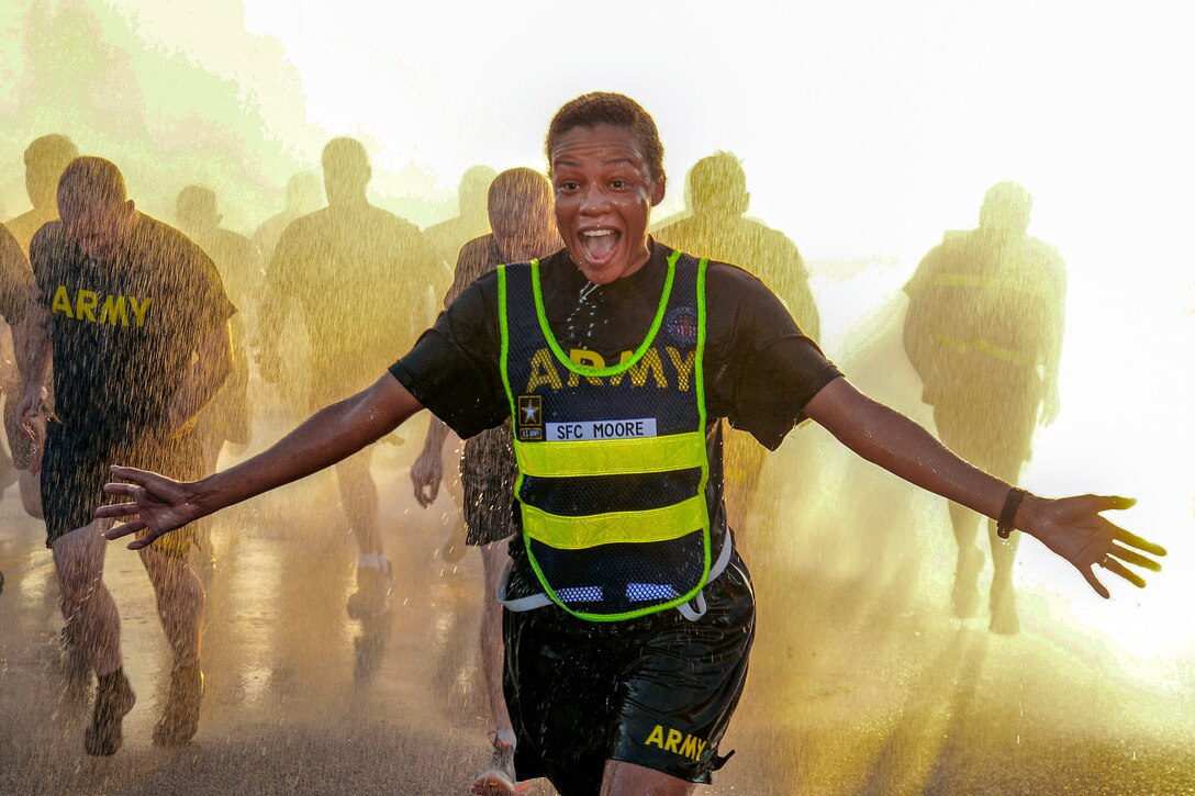 A smiling soldier holds out her arms while running through droplets of water ahead of other runners.
