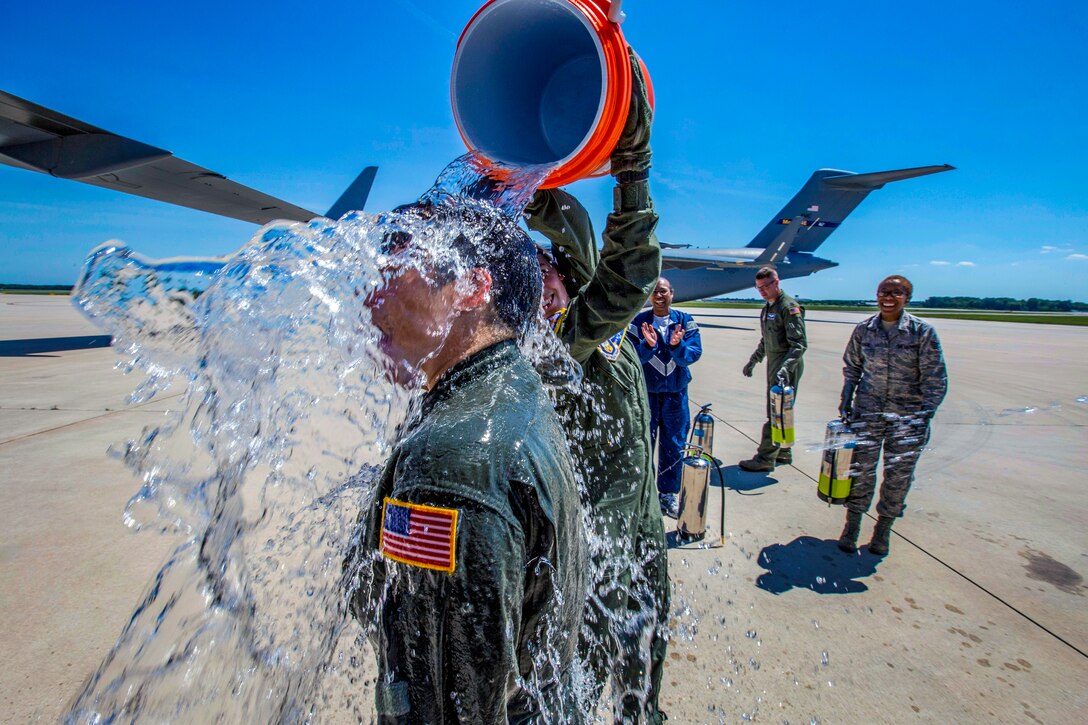 An airman empties a water bucket over a fellow airman's head.