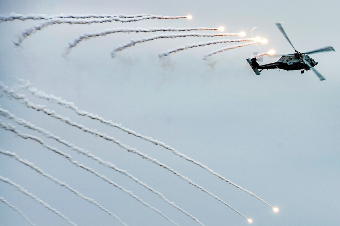 Flares burst in a linear pattern in the sky behind a helicopter firing them.