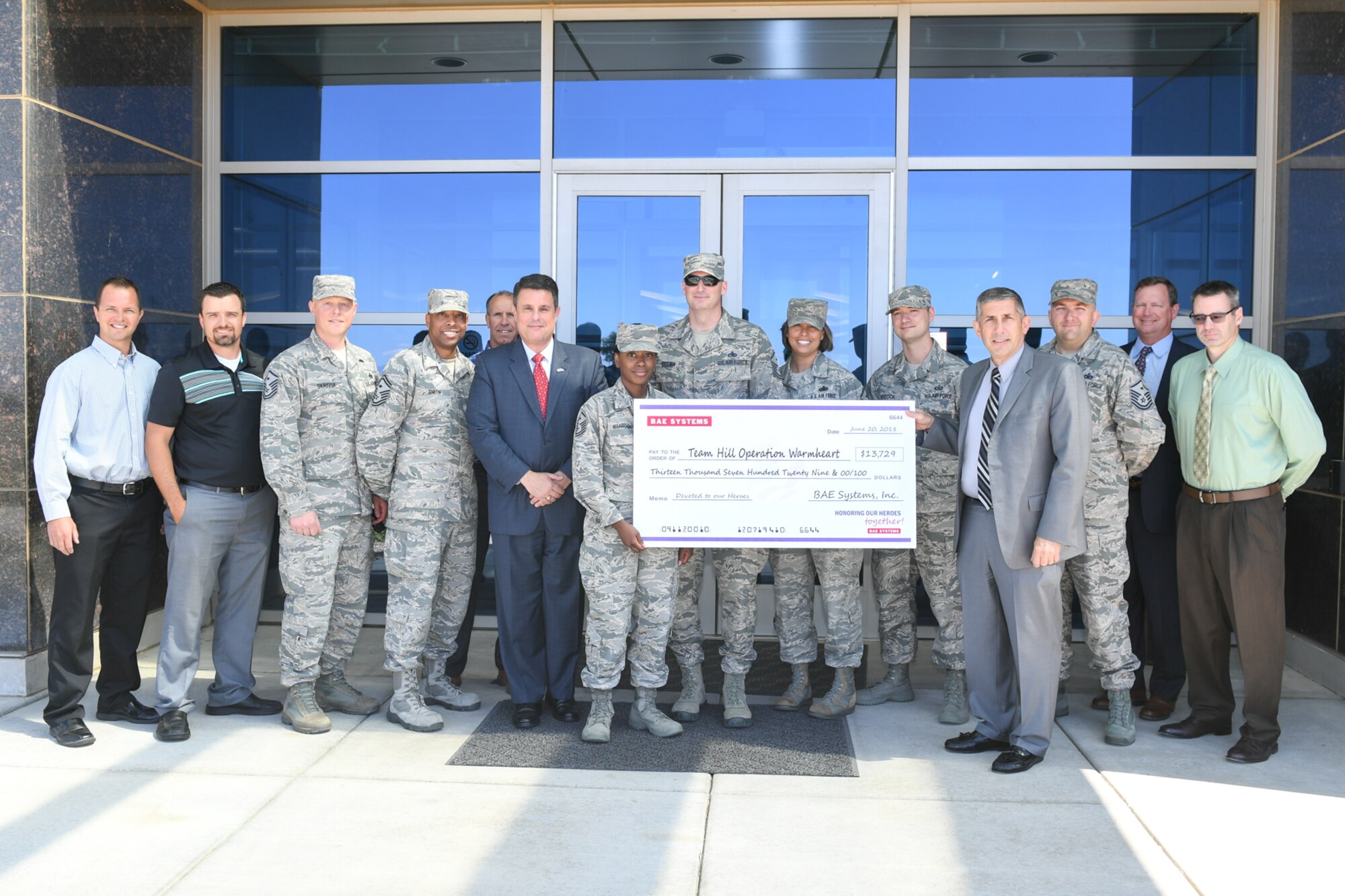 Randy Tymofichuk (right), Program Director of BAE Systems Inc., and Peter Trainer (left), Vice President/General Manager of Air Force Solutions, present a check to members of Hill Air Force Base, Utah, First Sergeants Group June 20, 2018. BAE Systems employees raised $13,729 for Hill AFB's Operation Warm Heart, which provides emergency grants to local military members and their families during times of need. (U.S. Air Force photo by Cynthia Griggs)