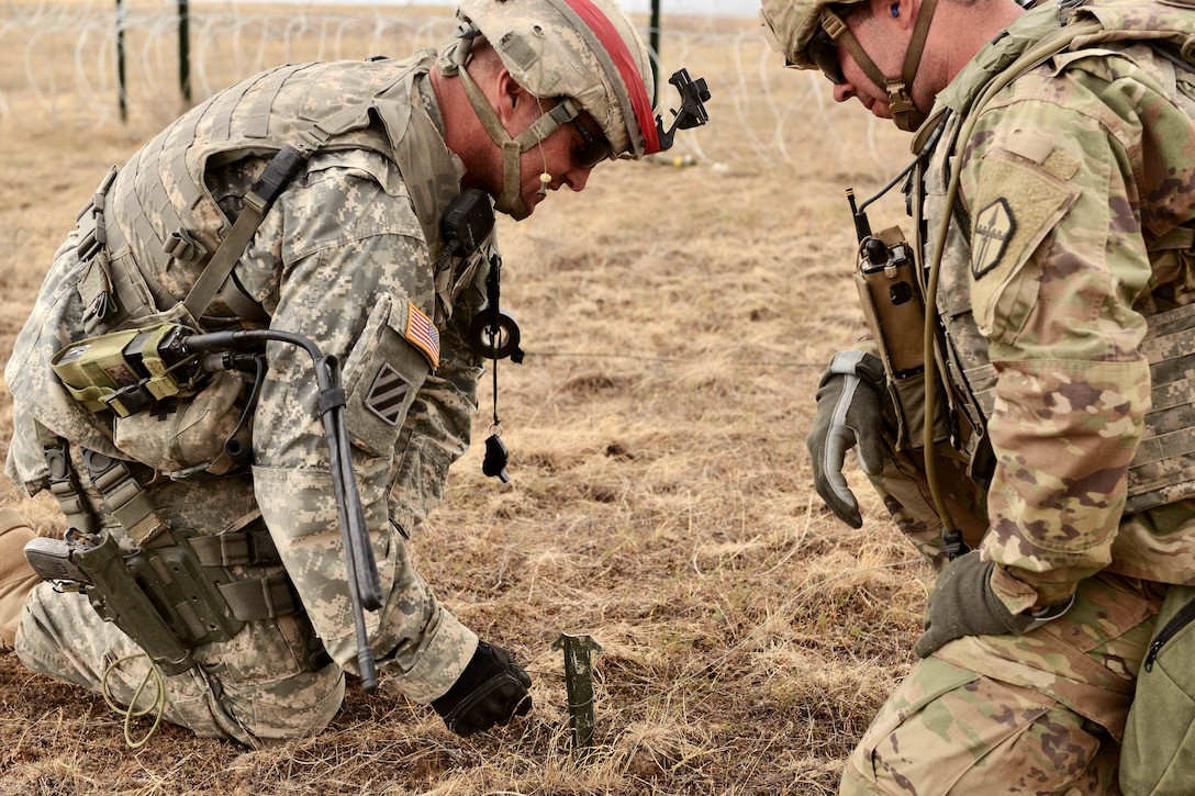 A soldier wraps shock tube around a guide stake and instructs a team member during the training.