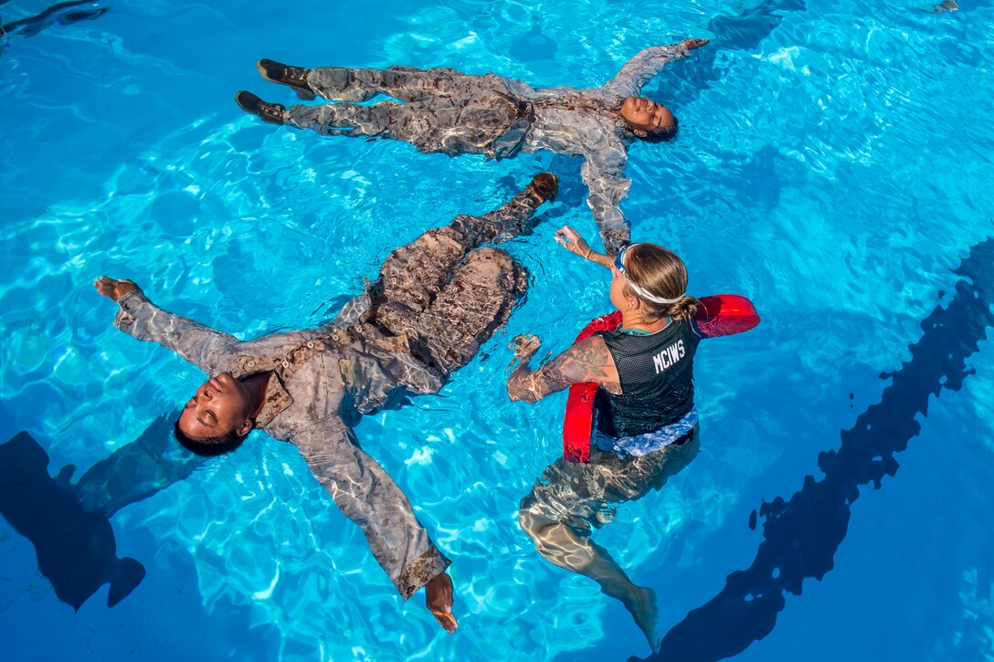 Two Marines float on their backs in a pool, as an instructor treads water and observes.