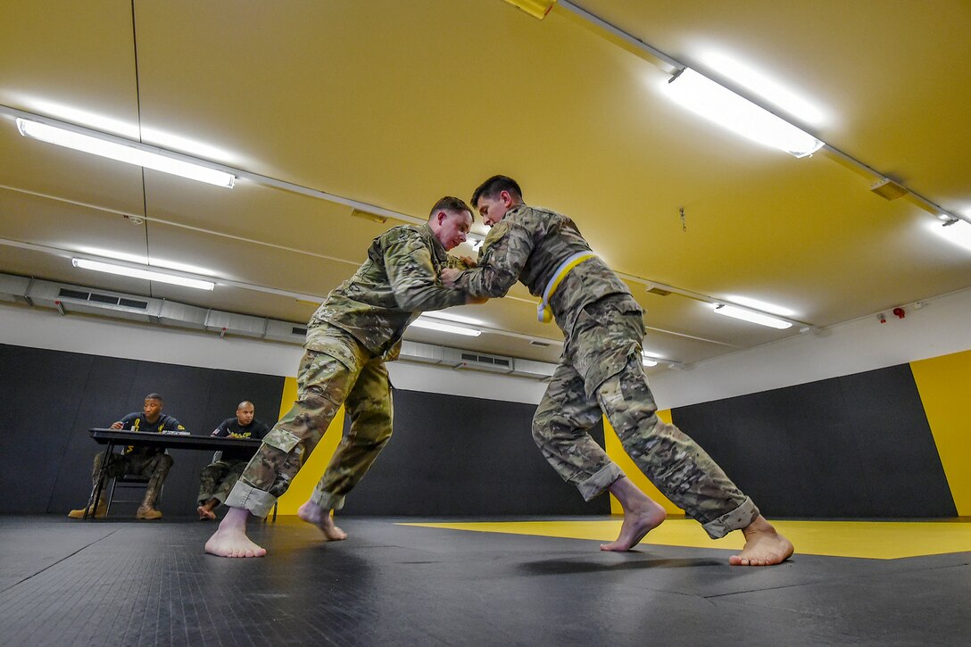 Soldiers grapple in a gym with yellow walls.
