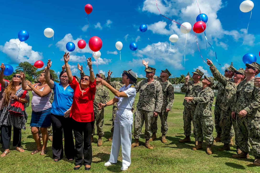 Civilians and service members release red, white and blue balloons in a field outside.