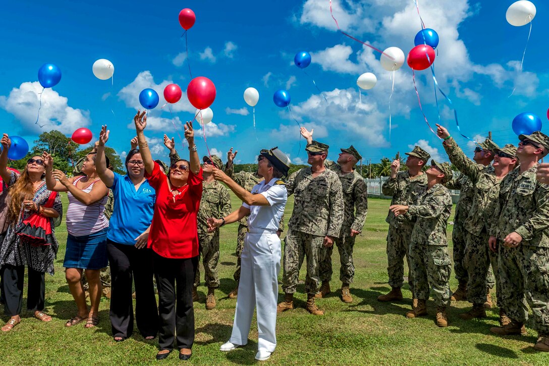 Civilians and service members release red, white and blue balloons in a field outside.