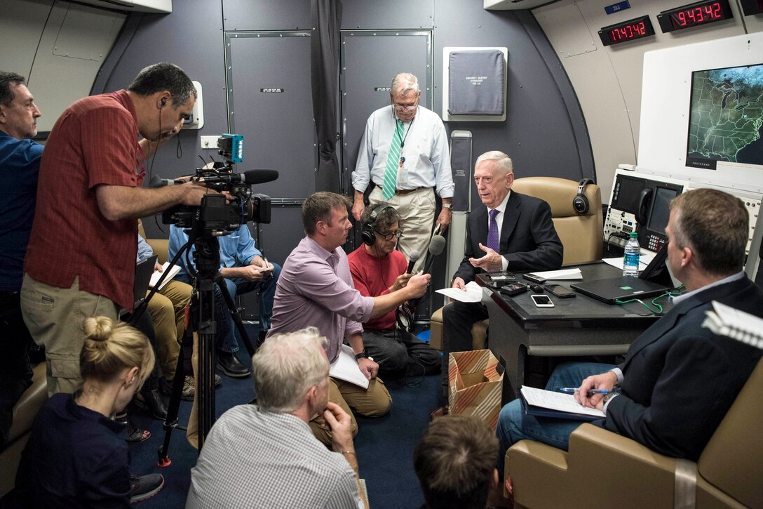 Defense Secretary James N. Mattis speaks to reporters in the cabin of an aircraft.