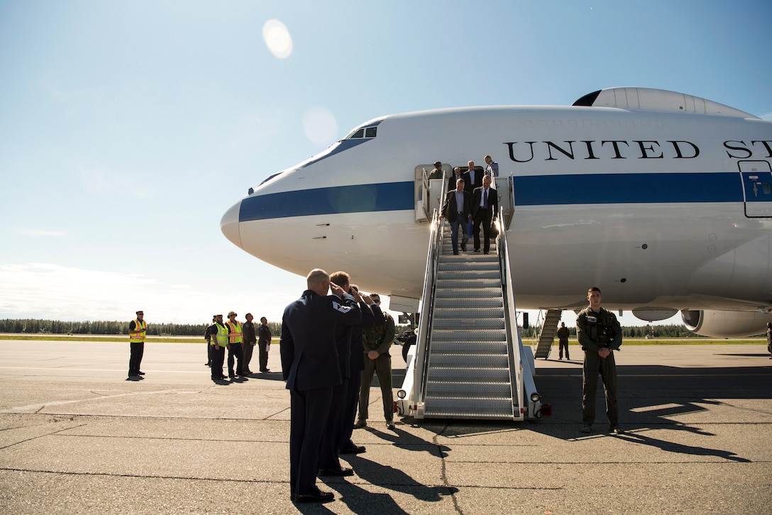 Defense Secretary James N. Mattis and U.S. Sen. Dan Sullivan disembark from an aircraft as saluting officials wait on a flightline.