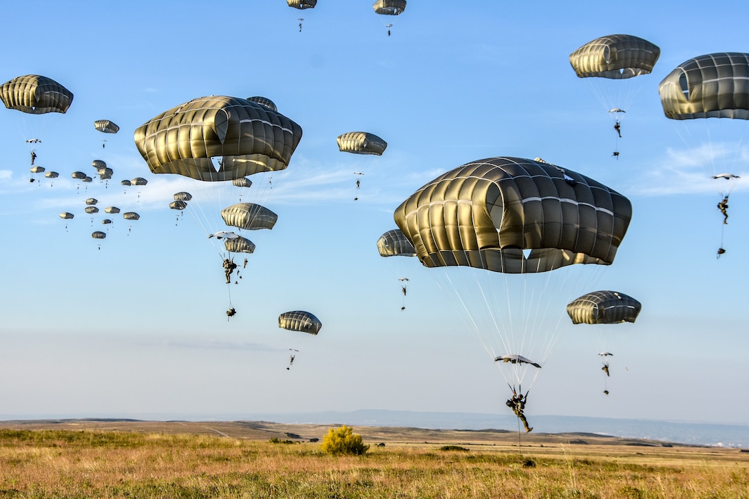 American and Spanish paratroopers land in a field using parachutes.