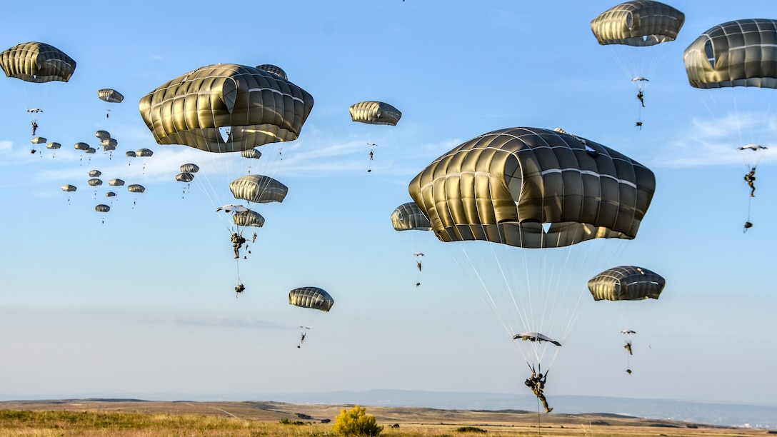 American and Spanish paratroopers land in a field using parachutes.