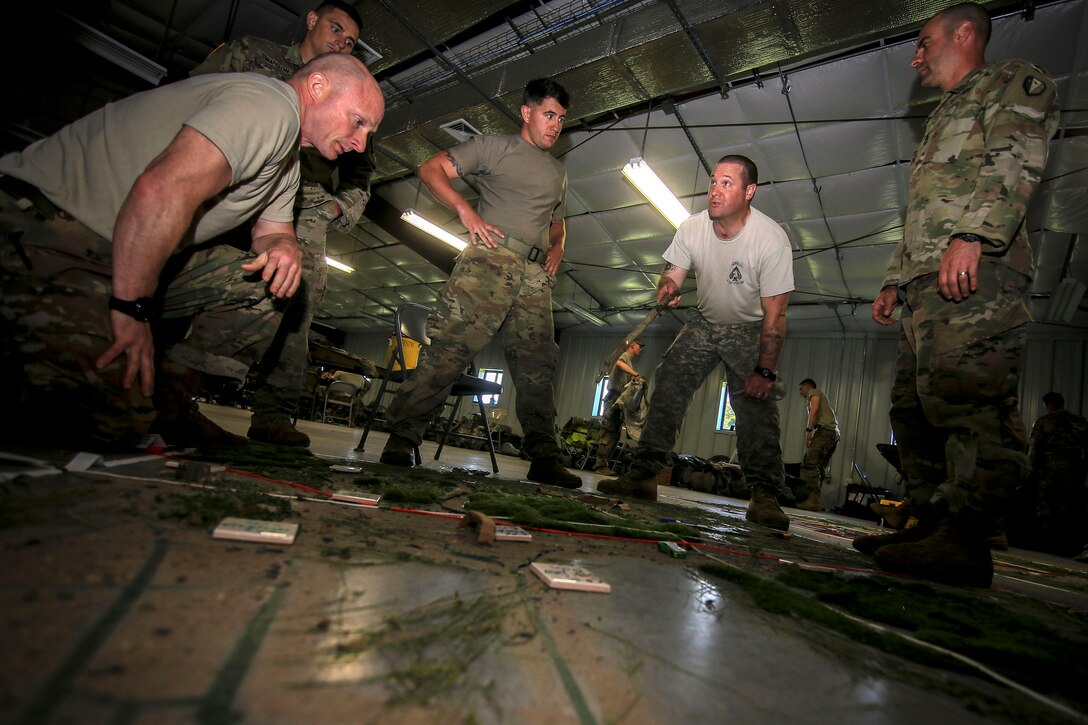 Soldiers plan out a training mission on a sand table.