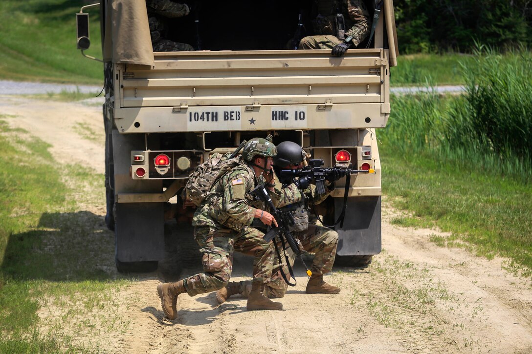 Soldiers shelter behind a tactical vehicle to look for enemy troops.