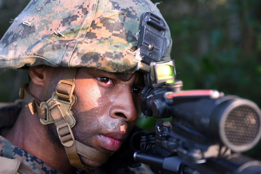 A Marine looks through a scope attached to a gun.