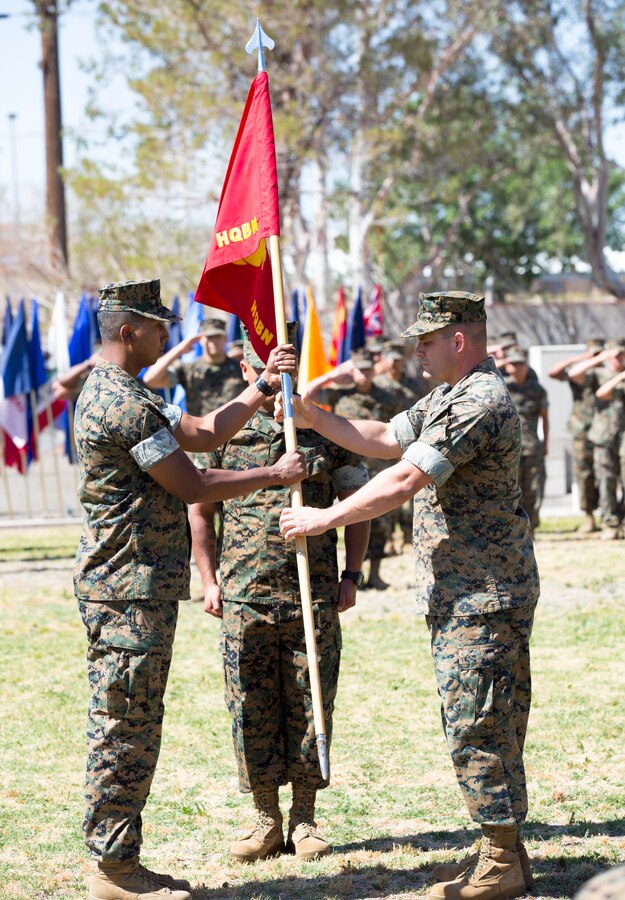 Maj. Alfredo Romero (right), outgoing Headquarters Company commanding officer, passes the unit colors to Captain Adam Rahman, incoming commanding officer during a change of command ceremony June 25. Rahman will also maintain his post as the S-6 Deputy Director, while Romero is slated to take the helm as the S-3 Operations Officer.