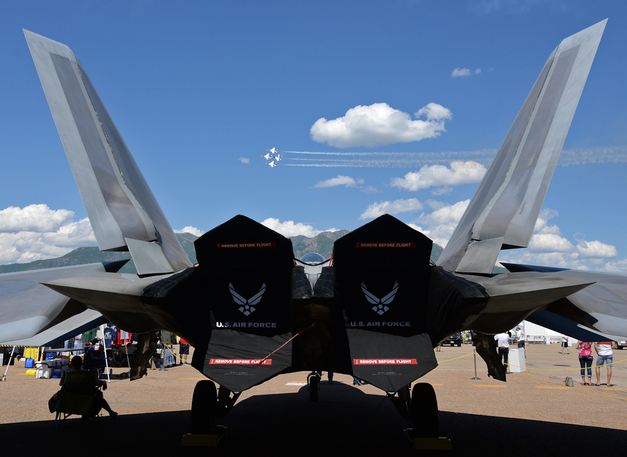 The U. S. Air Force Thunderbirds demonstration squadron in the diamond formation passes between the vertical stabilizers of an F-22 Raptor during the Warriors over the Wasatch Air and Space Show  June 23, 2018, at Hill Air Force Base, Utah, 2018. The Raptor was part of the static displays put out  by the Ogden Air Logistics Complex for air show visitors to view and photograph.  (U.S. Air Force photo by Alex R. Lloyd)