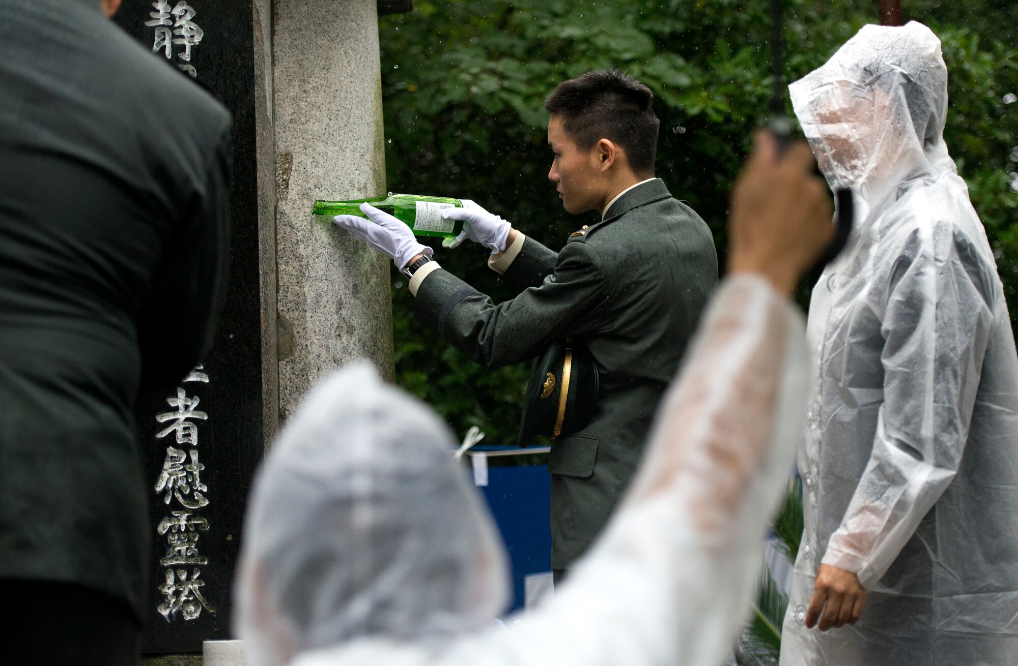 A Japanese military member pours sake onto the Japanese memorial