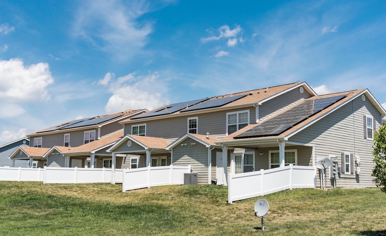 Two duplex housing units and white fences and solar panels on the roof.