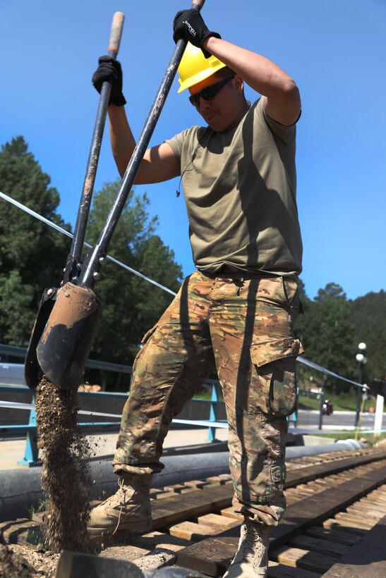 A soldier uses a post hole digger to remove dirt from a project site.