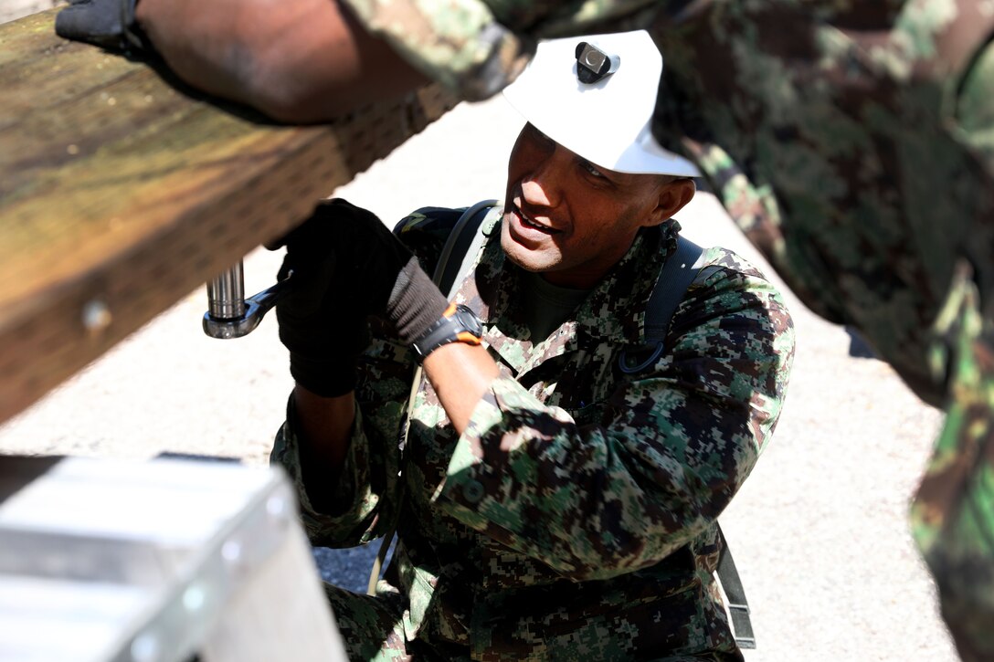 A Suriname soldier uses a ratchet wrench to secure a joist during a bridge repair project.
