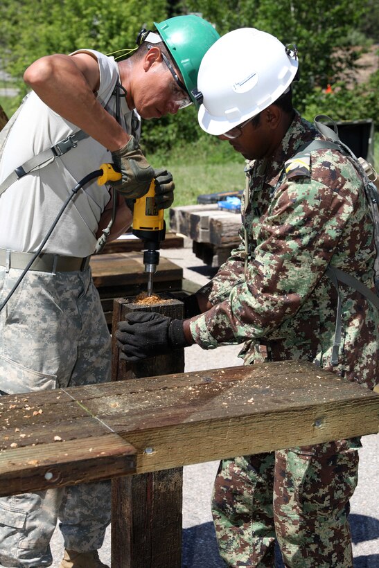 A U.S. and Suriname soldier drills holes into a support beam during a bridge repair project.