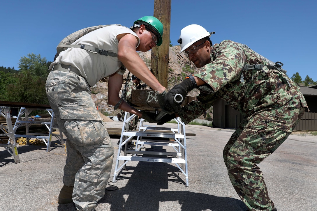 A U.S. soldier and a Suriname soldier secure a joist during a bridge repair project.