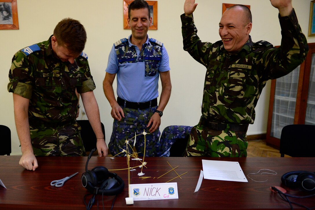 Three Romanian Air Force students react as their structure falls over during a strategic thinking exercise during the first-ever senior noncom missed officer mobile education course June 8 to 22, 2018, at Boboc Air Base, in Buzău, Romania. The SNCOA mobile training team partnered with the Inter-European Air Forces Academy to provide a two-week course, condensed from the full five-week course held at Maxwell Air Force Base- Gunter Annex, Alabama. (U.S. Air Force photo by Tech. Sgt. Staci Kasischke)