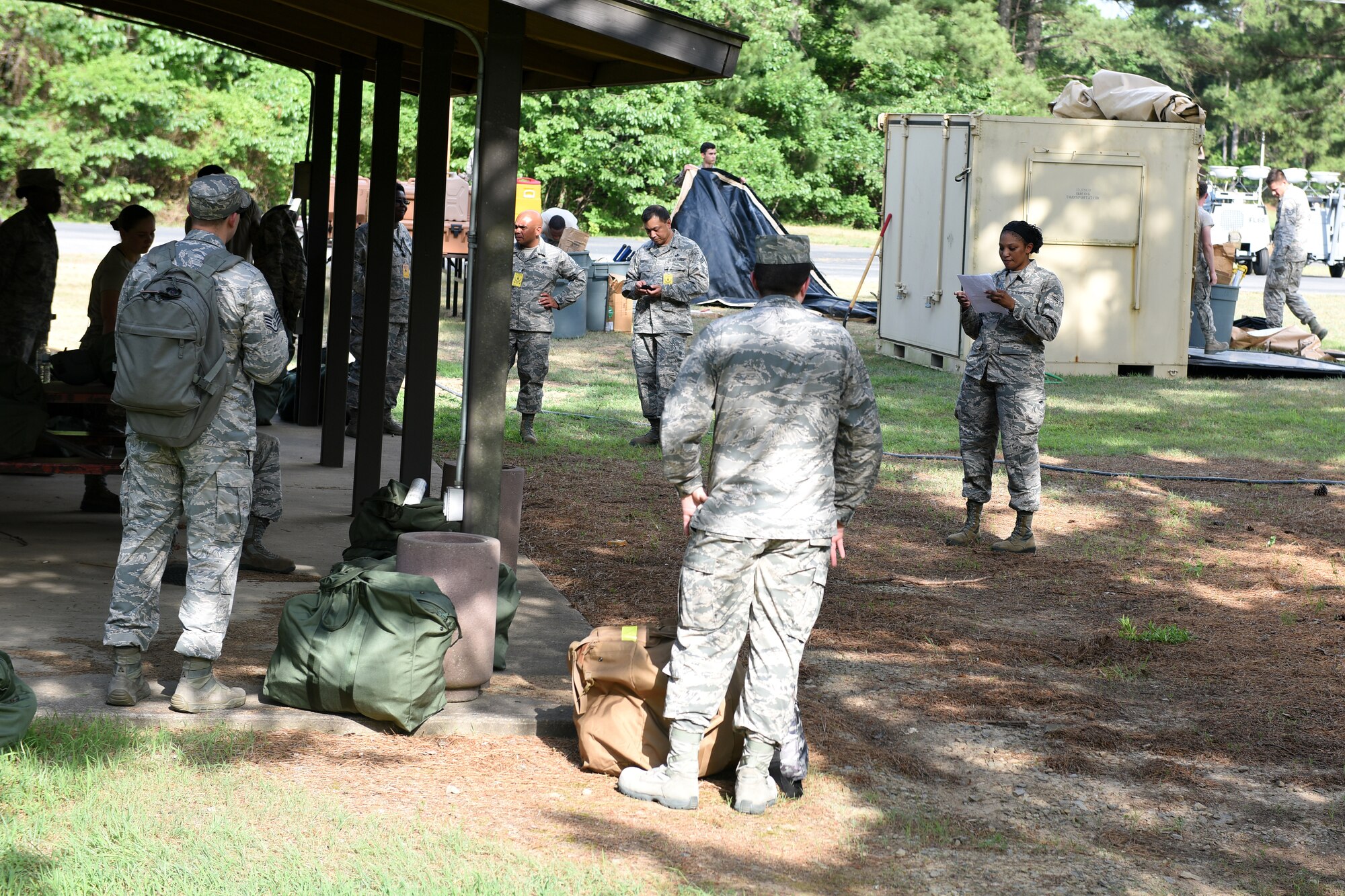People in uniforms participate in an exercise wearing various equipment and gas masks.
