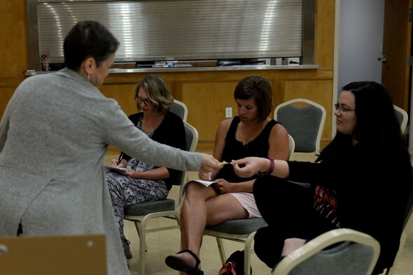 Three women sit in chairs and write on sticky notes.