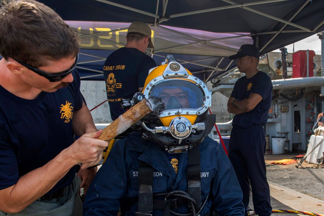 A U.S diver cleans a Royal Thai navy diver headgear while preparing for a joint dive training.