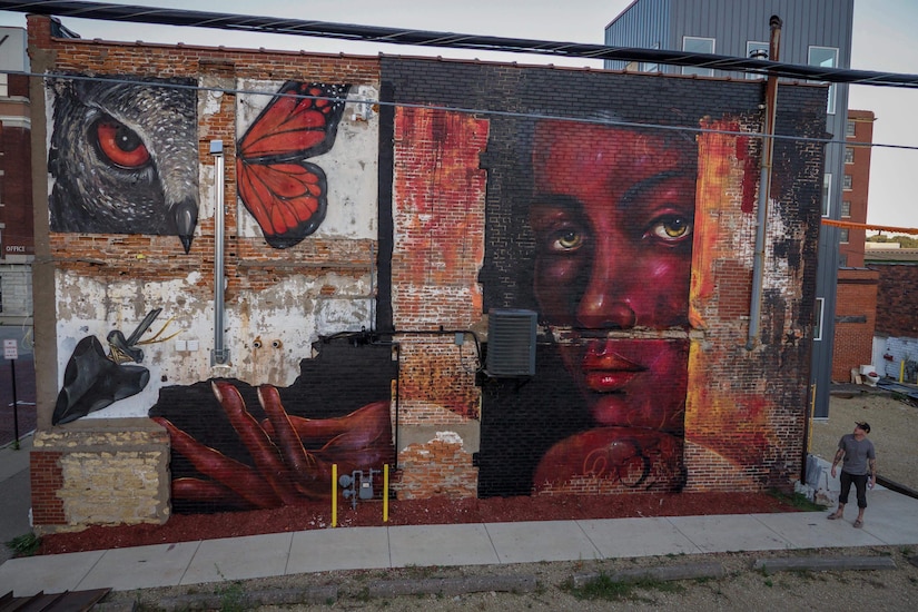 Airman stands next to large mural.