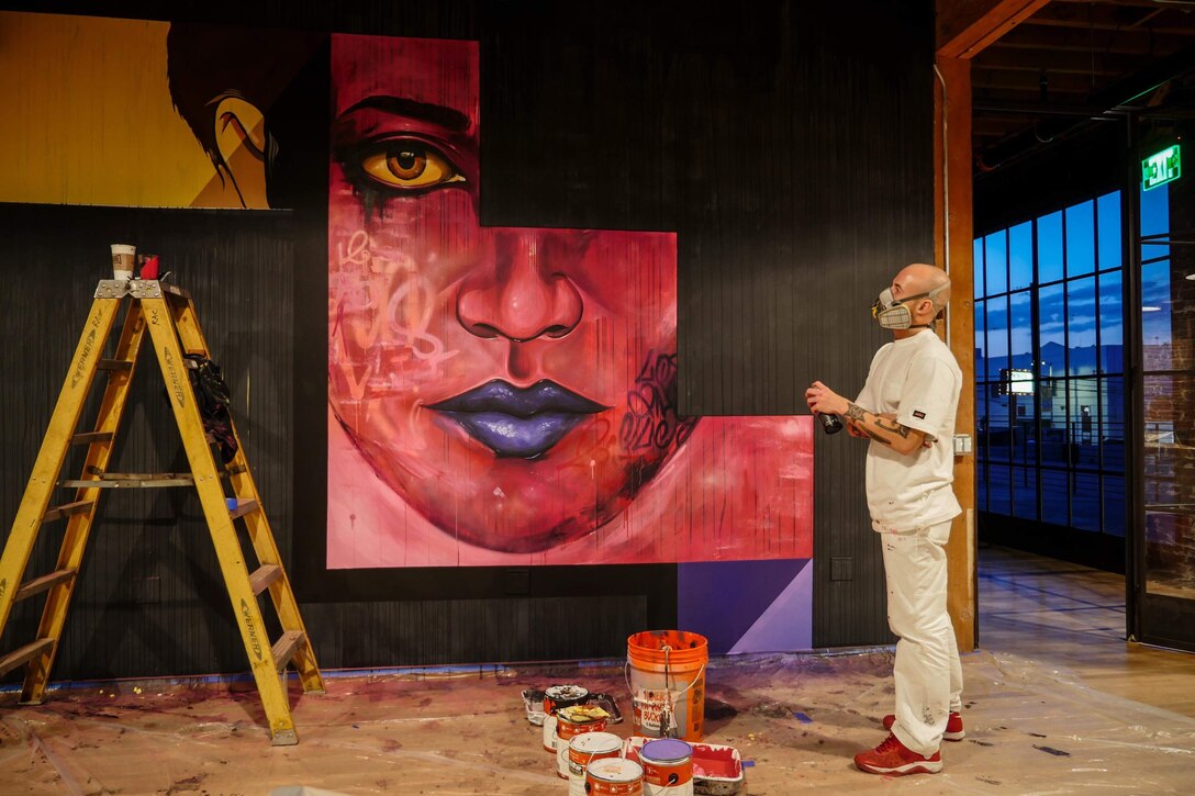 Airman paints a large mural of a face.