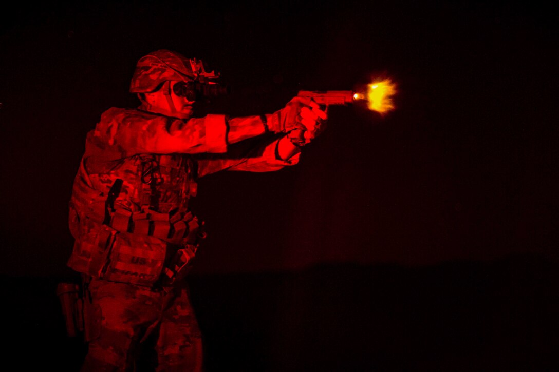 A soldier fires a handgun at night.