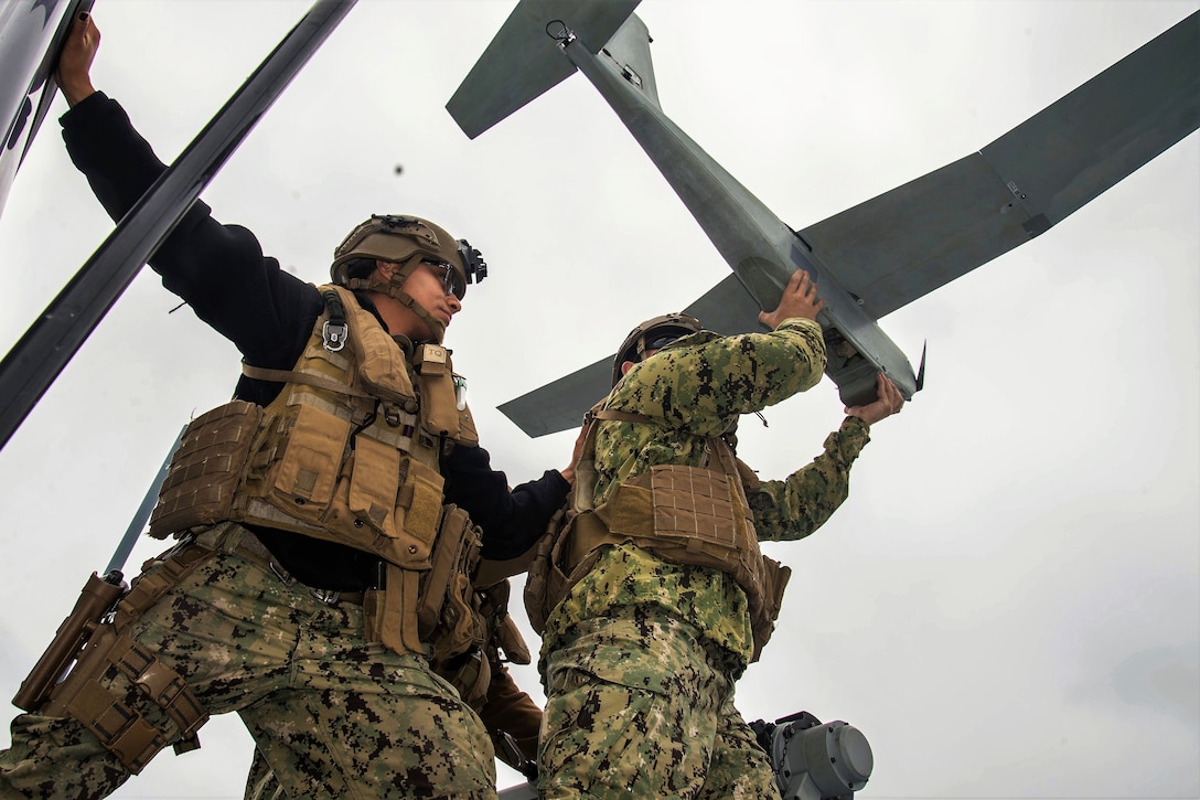 A sailor steadies a team member before launching an unmanned aerial vehicle.