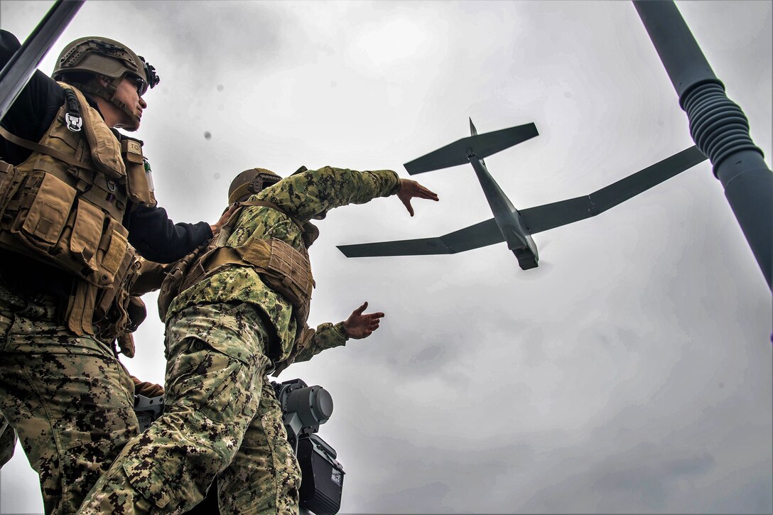 A sailor steadies a team member before launching an unmanned aerial vehicle.
