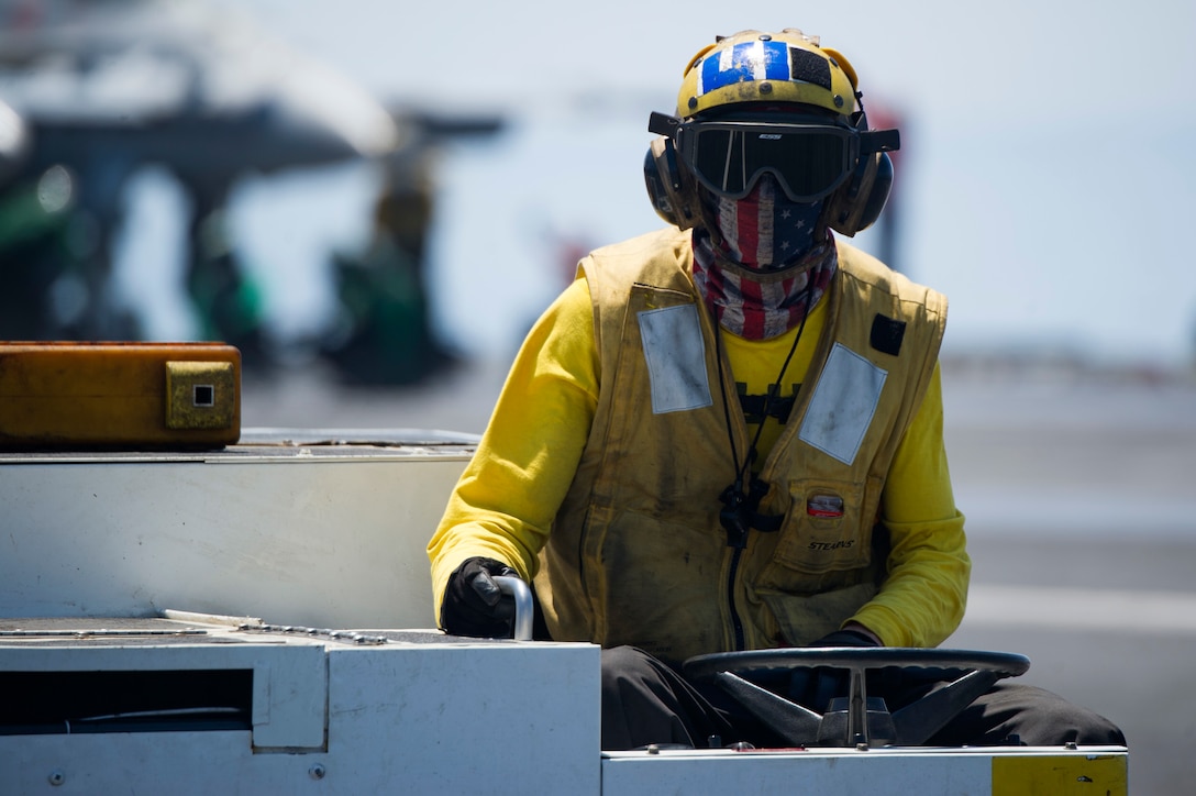 A sailor operates an aircraft tractor on the flight deck.