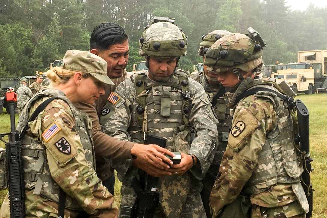 Five soldiers stand together looking at an electronic device.