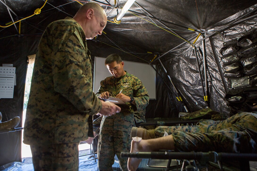 Lt. Cmdr. Martin Kelly (left), a system battalion surgeon, and Chief Augusto Gador (right), the battalion chief, both with 2nd Battalion, 24th Marine Regiment, 23rd Marines, 4th Marine Division, administer aide to a Marine with blistered heals after a conditioning hike during Mountain Exercise 3-18, at Mountain Warfare Training Center, Bridgeport, Calif., June 21, 2018.
