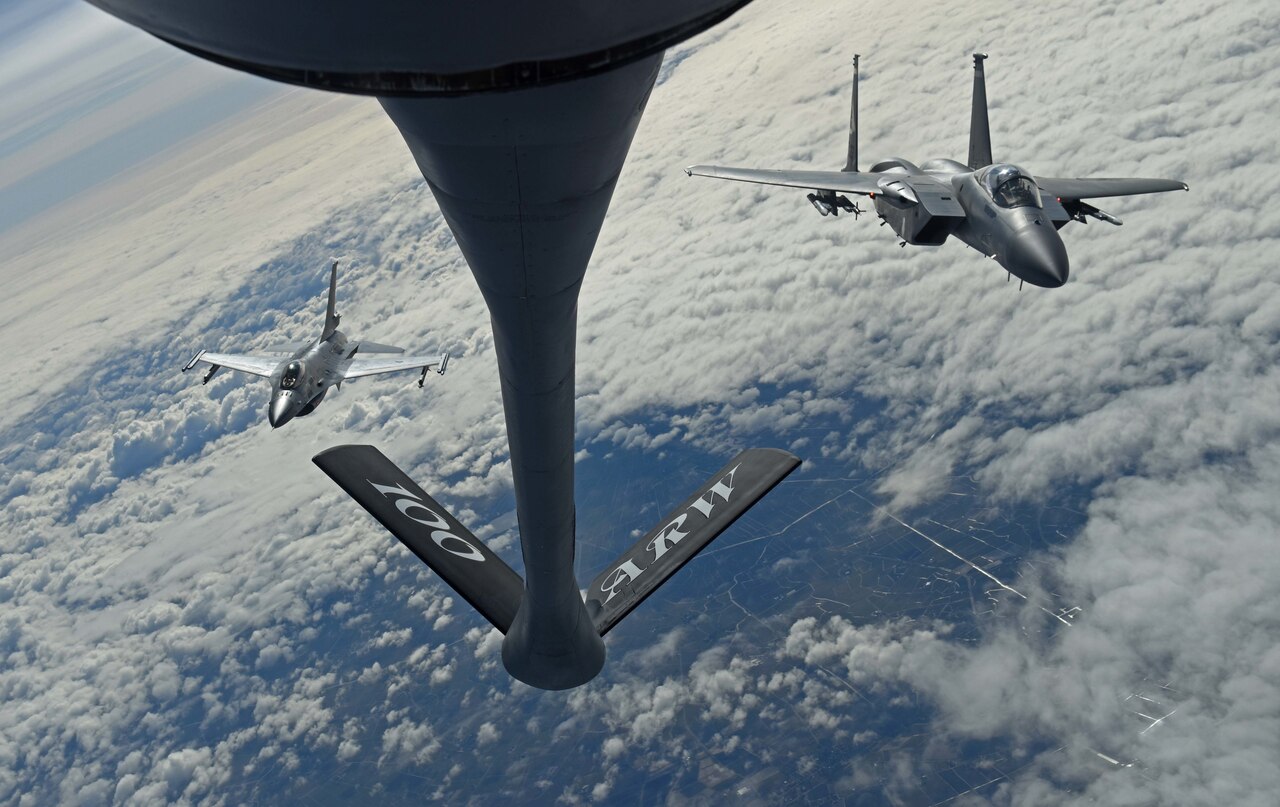 Fighter jets fly behind aerial refueling tanker.