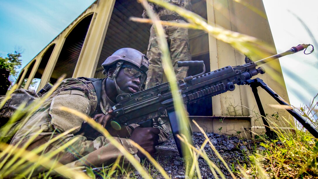 A soldier lays on the ground and another stands.