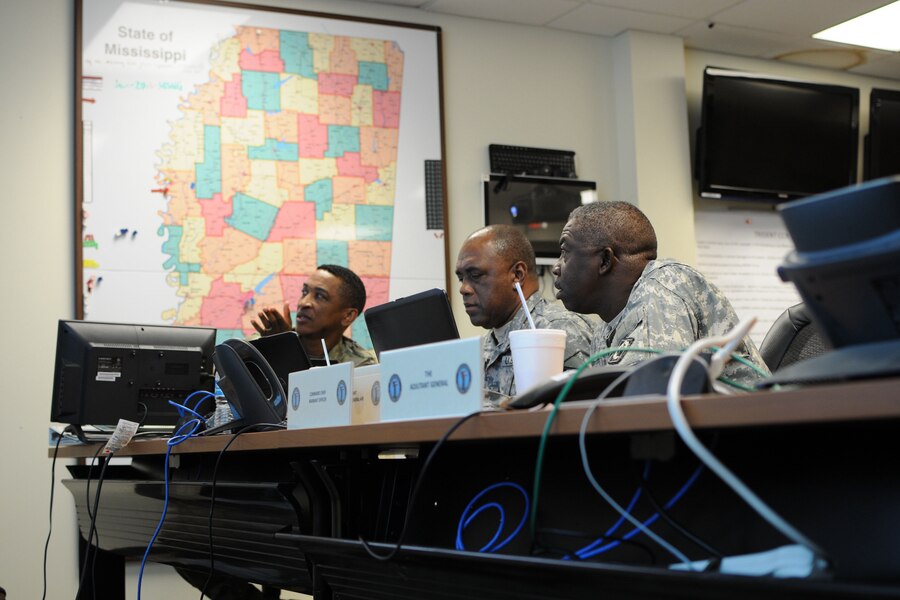 Soldiers sit behind a desk looking a computers.