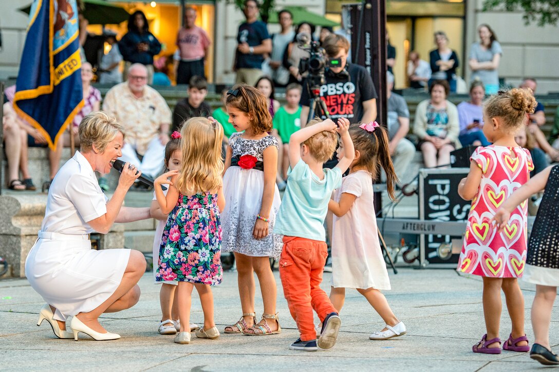 A sailor kneels down while singing to children.