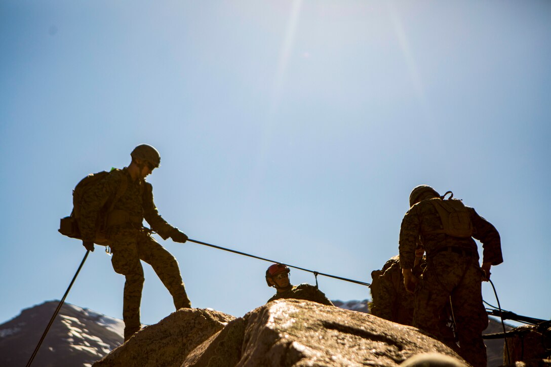 Marines are silhouetted by the sun as they rappel down a cliff.