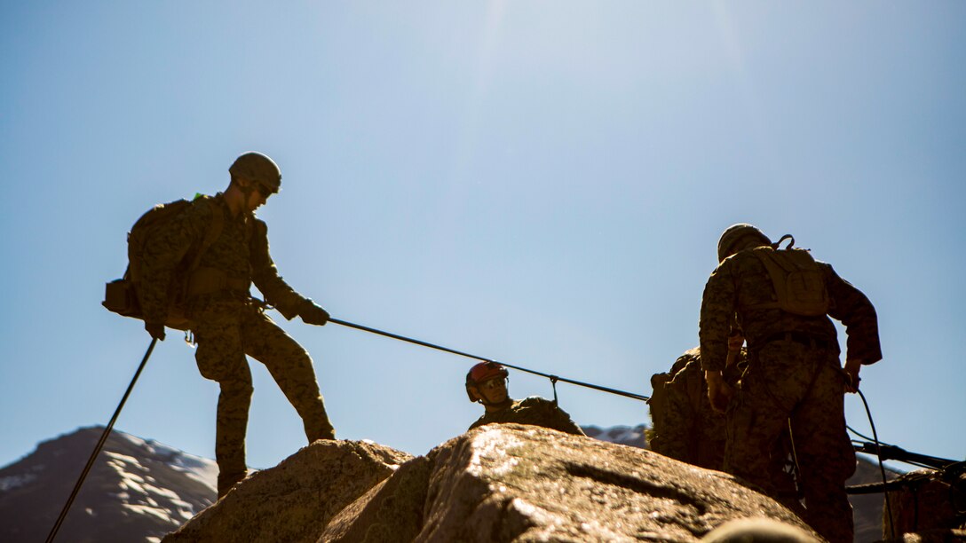 Marines are silhouetted by the sun as they rappel down a cliff.